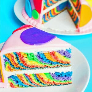 Sliced one pan rainbow layer cake served on white plate.