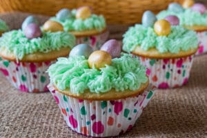 ¡Los deliciosos cupcakes de canasta de Pascua están cubiertos con glaseado de crema de mantequilla verde 'hierba' y cubiertos con mini huevos de chocolate con leche Cadbury!