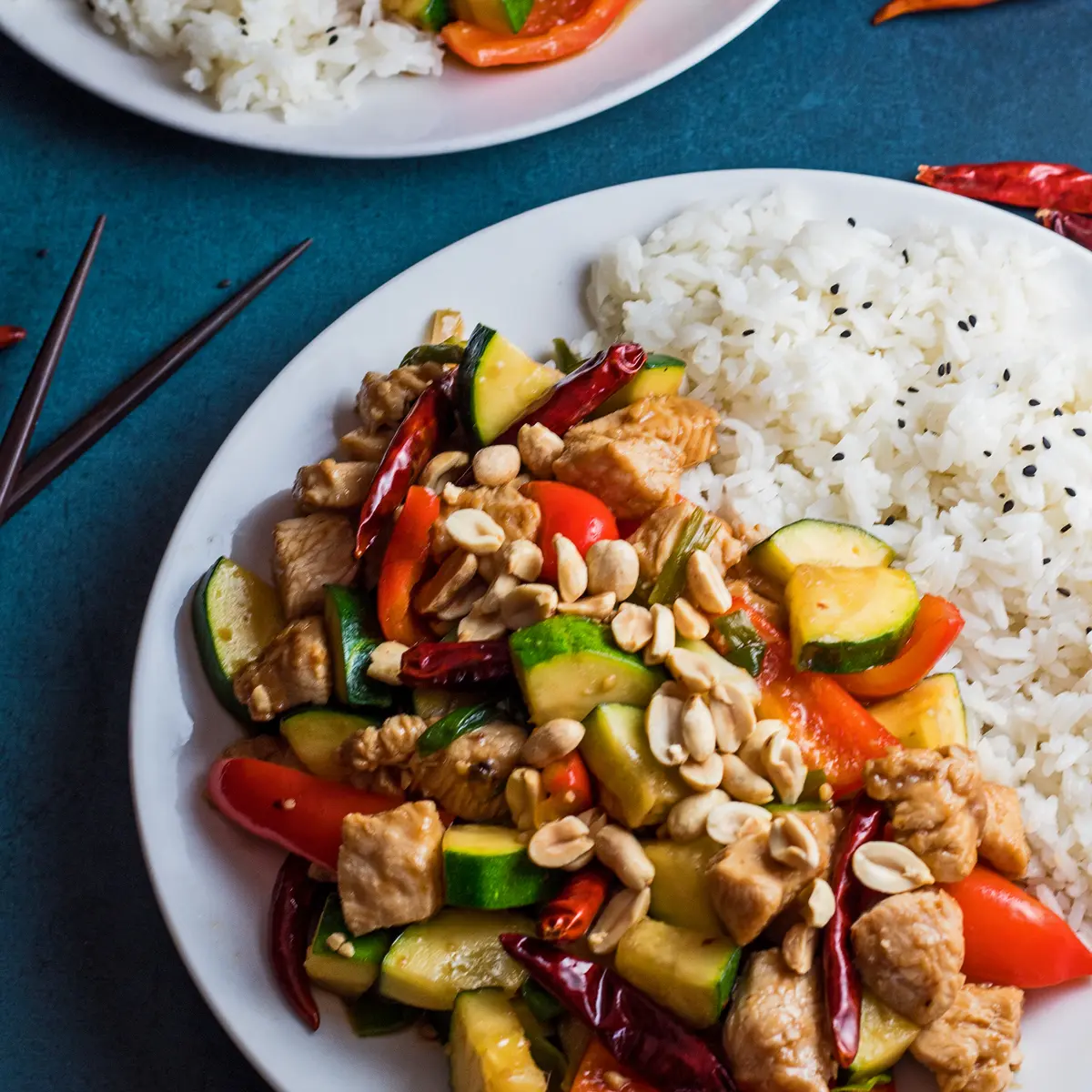 Голямо квадратно изображение на пиле Panda Express Kung Pao, сервирано върху бяла чиния с ориз на син фон.