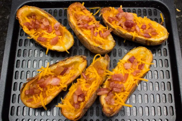 Air fryer potato skins after being cooked for 10 minutes and with grated cheddar cheese and crumbled bacon added.