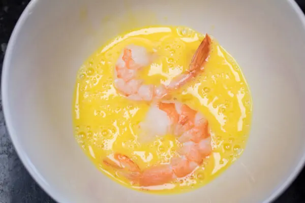 coating raw peeled shrimp with tail on in the whole egg mixture