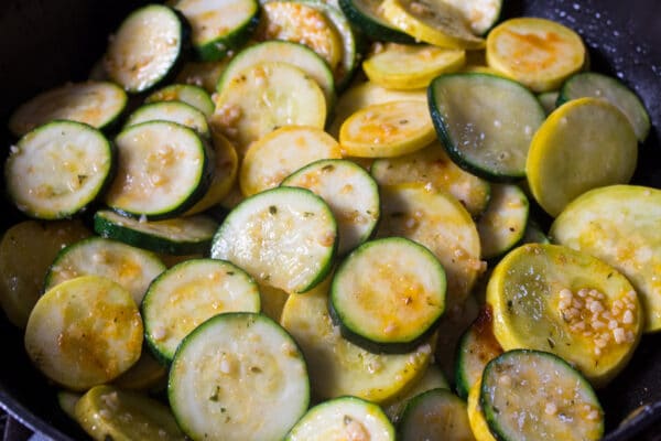 sliced zucchini and yellow squash being sauteed in the pan with garlic