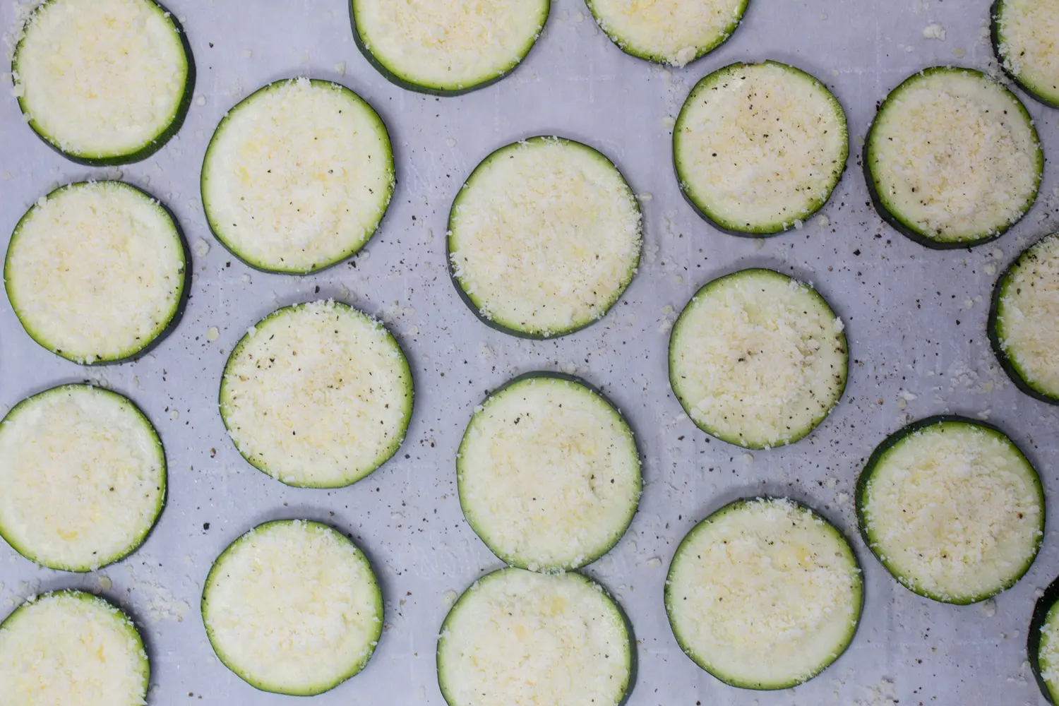zucchini sliced in rounds laid out on baking sheet and seasoned with salt and pepper then topped with grated parmesan cheese