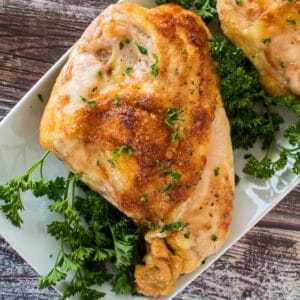Tender oven roasted bone in chicken breast garnished with fresh parsley on white plate.