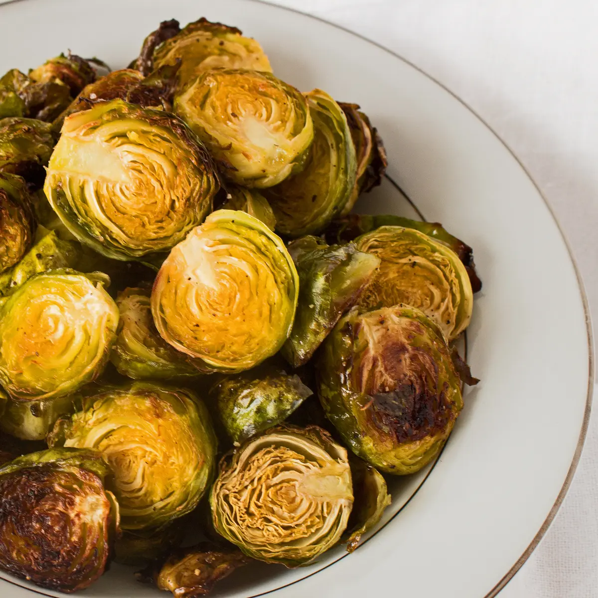 Roasted brussel sprouts showing golden caramelized color in a white serving bowl on white background