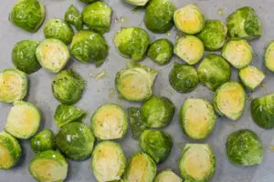 prepared brussel sprouts with olive oil and seasoning on parchment paper lined baking sheet and ready to roast in preheated oven