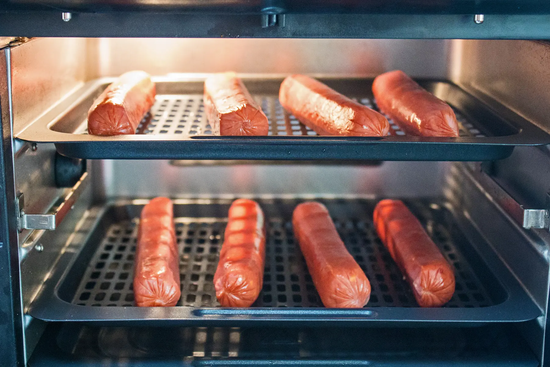 8 hot dogs set on convection oven style air fryer racks and placed in the oven after preheating, ready to cook.