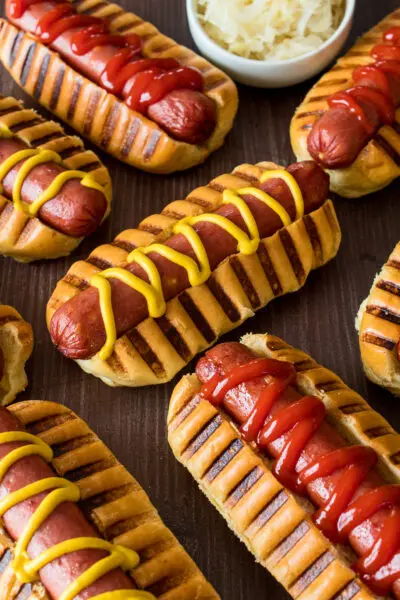 vertical image taken from the side with theketchup and mustard garnished air fryer hot dogs in the front and sauerkraut in the background