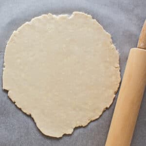 Large square overhead image of the rolled pie crust on light background with the rolling pin set next to the dough edge