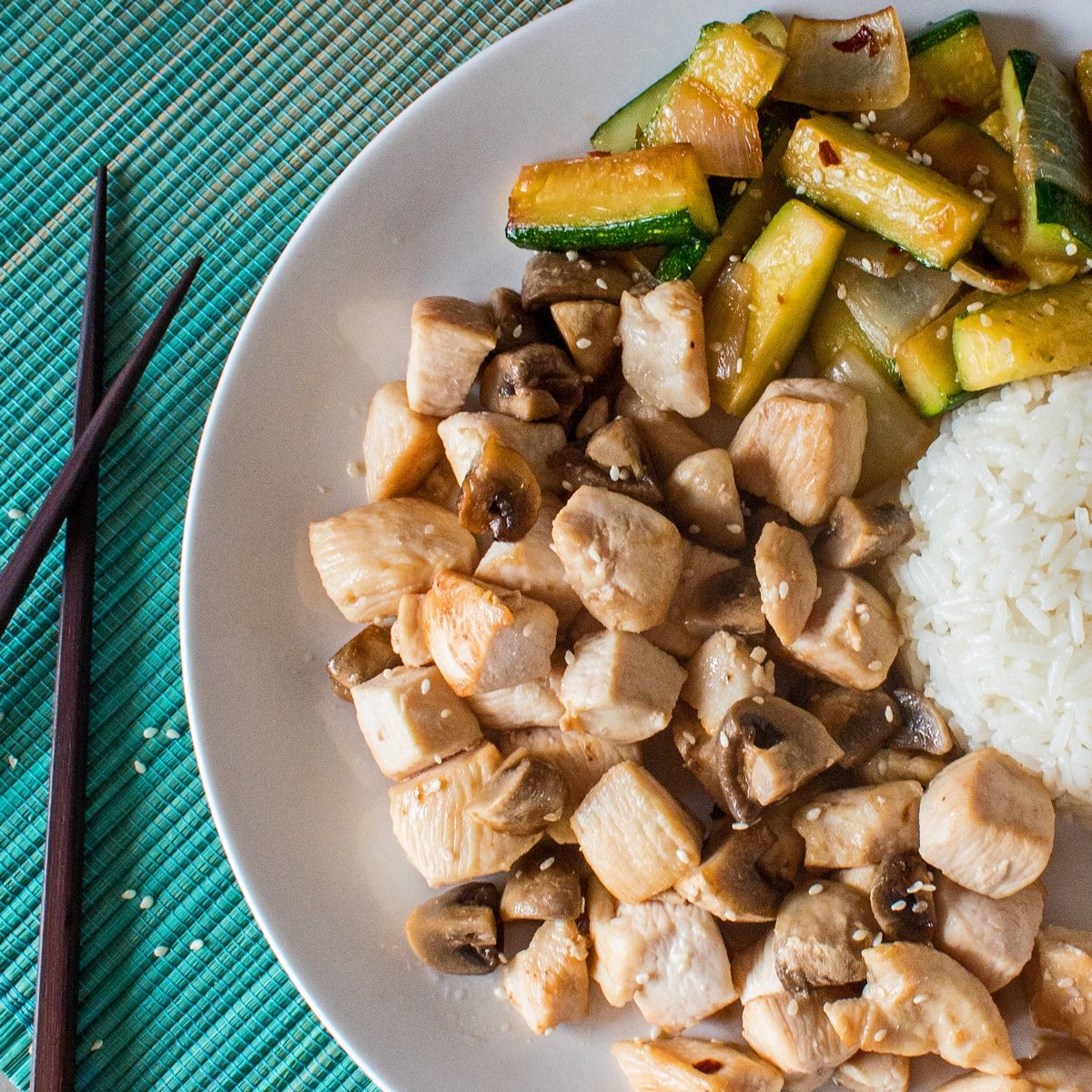 Pollo hibachi servido con calabacín hibachi y arroz en un plato blanco con fondo aqua ombre claro