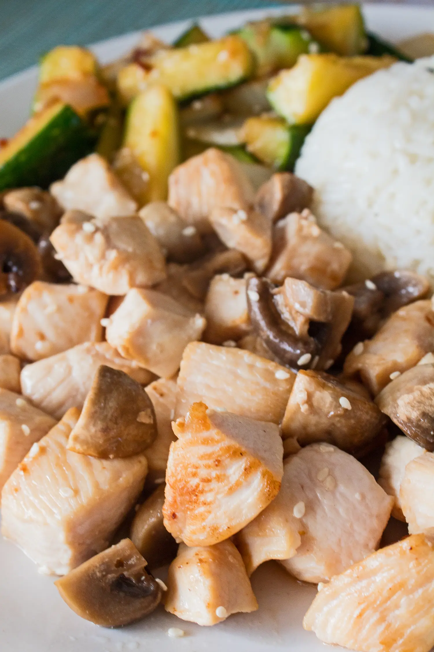 closeup view of hibachi chicken with mushrooms on a white plate with hibachi zucchini and rice in the background