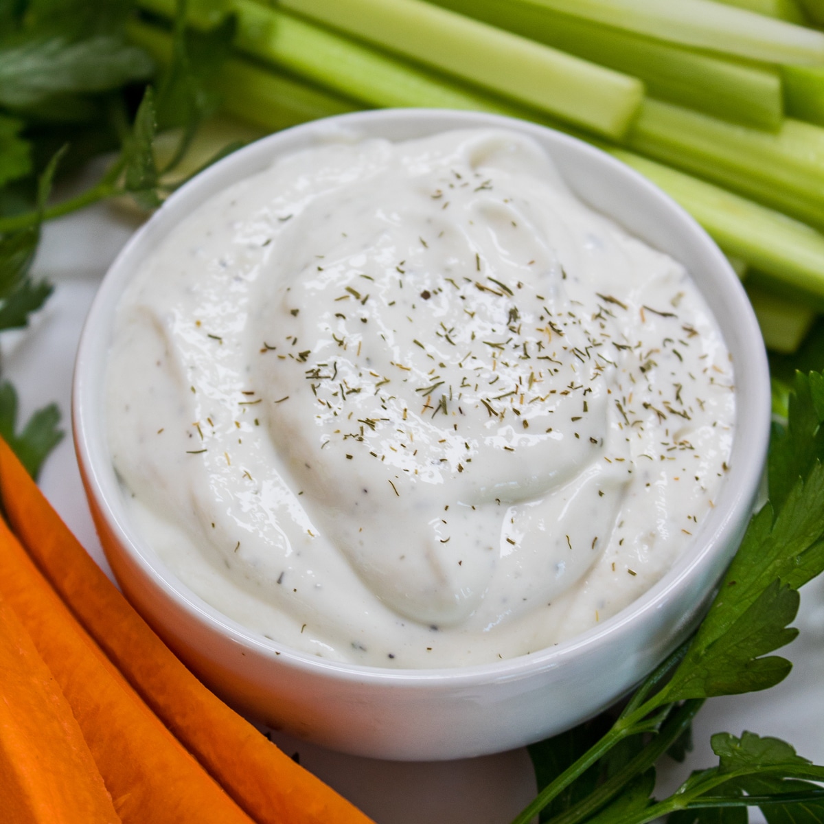 Overhead of homemade ranch dressing garnished with dried dill and served in a white bowl with carrots and celery.