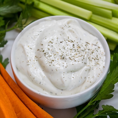 overhead of homemade ranch dressing garnished with dried dill and served in a white bowl with carrots and celery