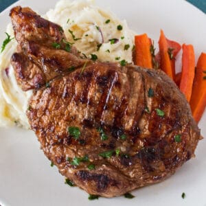 Single marinated grilled pork chop shown on a white plate with mashed potatoes and sliced carrots.