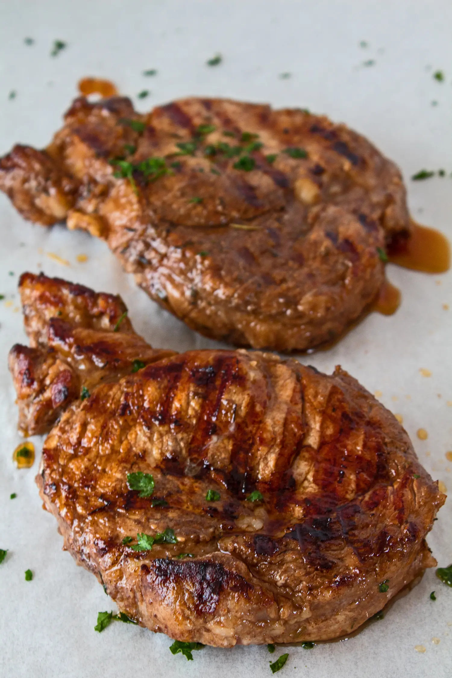 two marinated grilled pork chops shown on parchment paper while resting