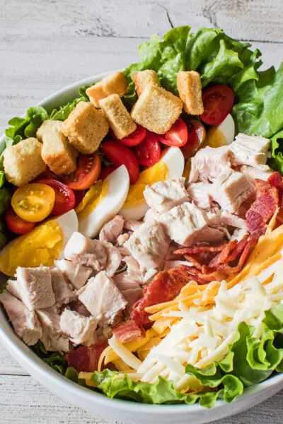 close up vertical image showing the layered turkey meat bacon cheeses had boiled eggs tomatoes and croutons on a bed of leaf lettuce