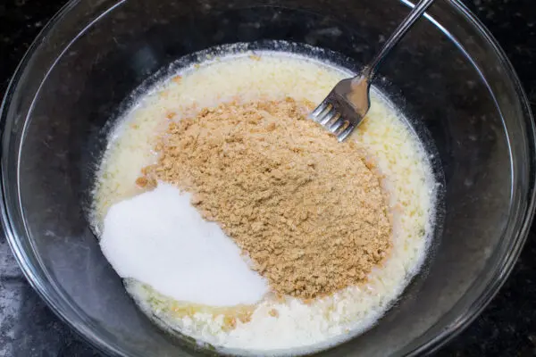crushed graham cracker crumbs with sugar and melted butter ready to be combined using a fork