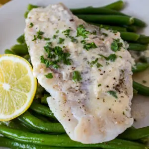 large square angled overhead image of foil packet grilled haddock served on a bed of green beans with lemon on the side