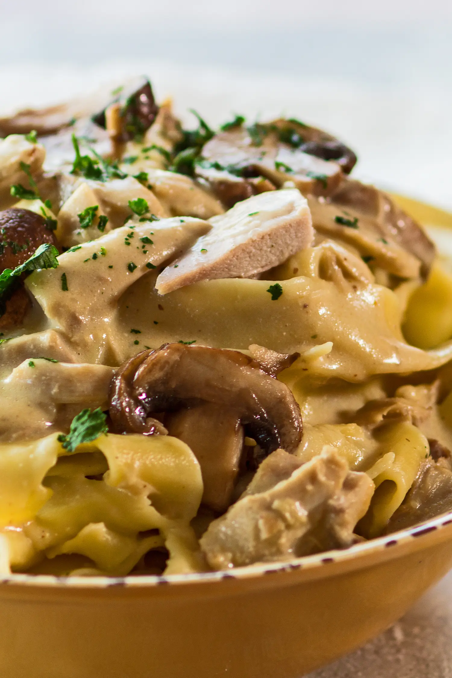 vertical image of the leftover turkey stroganoff with mushrooms served up in a light golden bowl