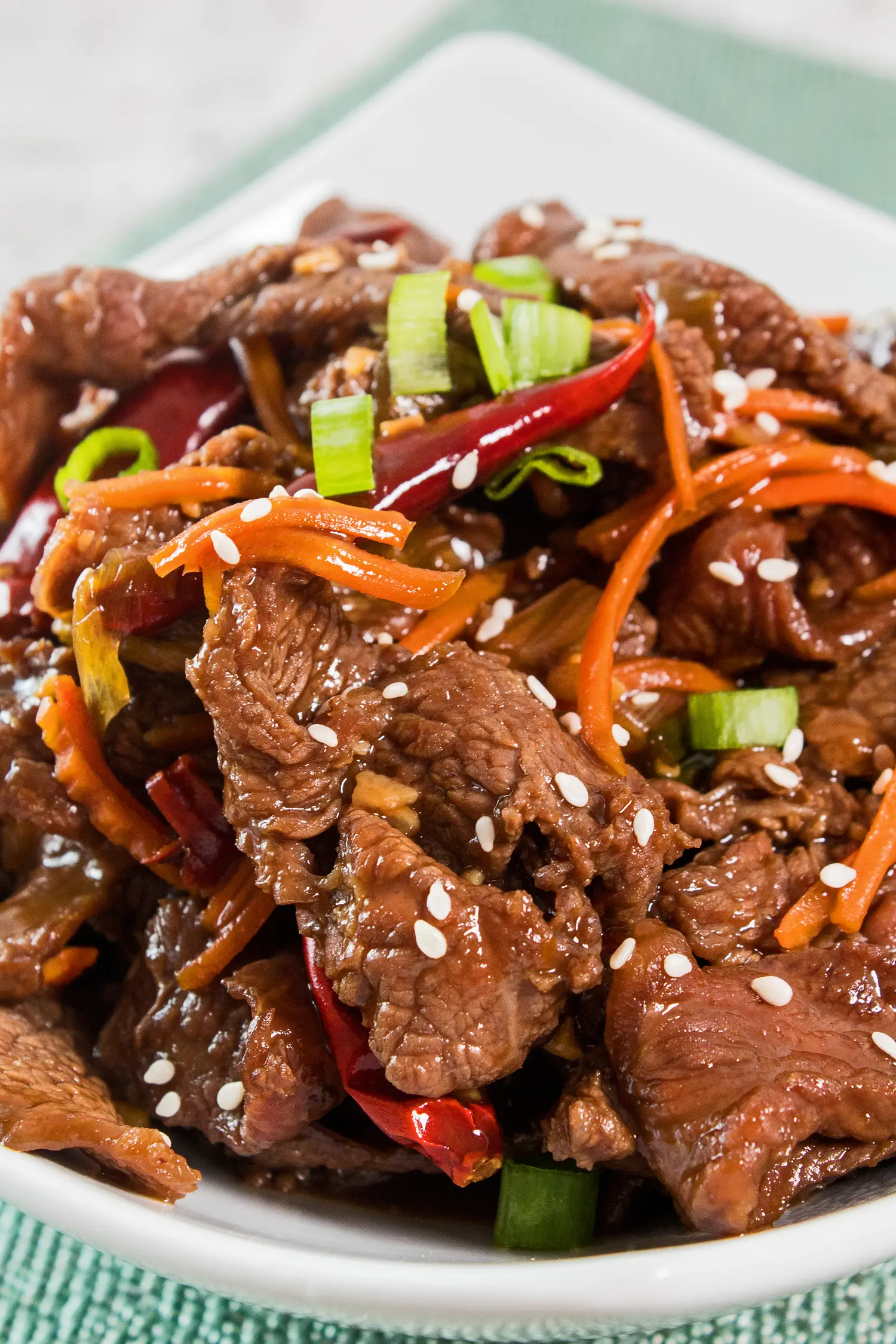 closeup vertical image of dished up mongolian beef garnished with sliced green onions and sesame seeds