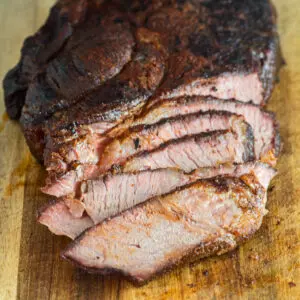 Square image showing tender juicy sliced smoked beef chuck roast after smoking on the cutting board.