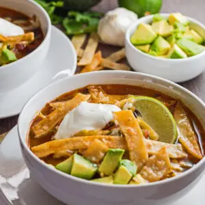 Large square perfect chicken tortilla soup with garnish served in white bowls.