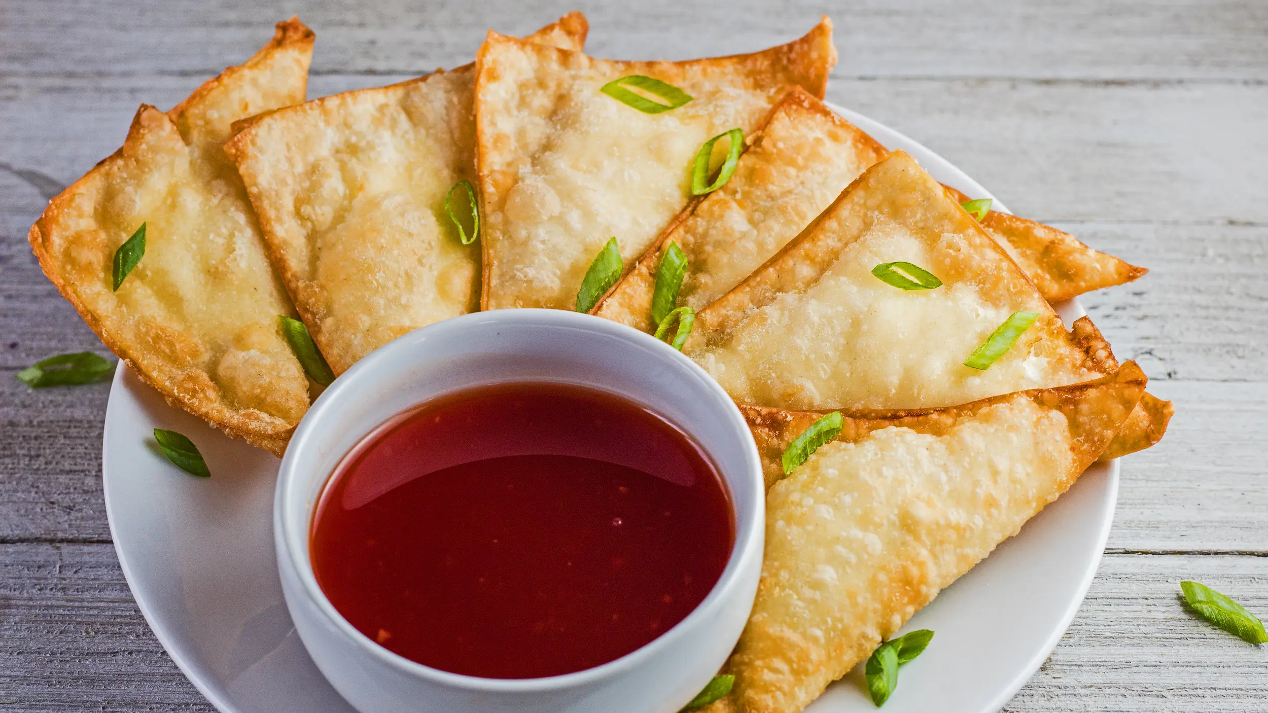 wide angled overhead image of the plated cream cheese wontons with sweet and sour sauce for dipping.