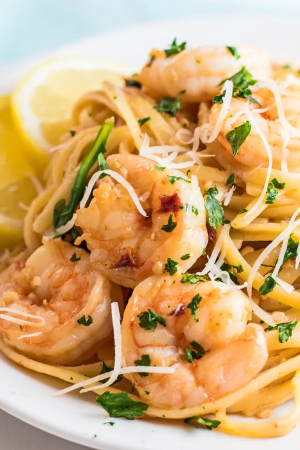tall closeup of the garlic shrimp pasta served on white dish with lemon wedges.