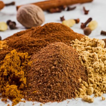 wide image of the ground spices poured onto a white background with whole spices for the pumpkin pie spice in background.