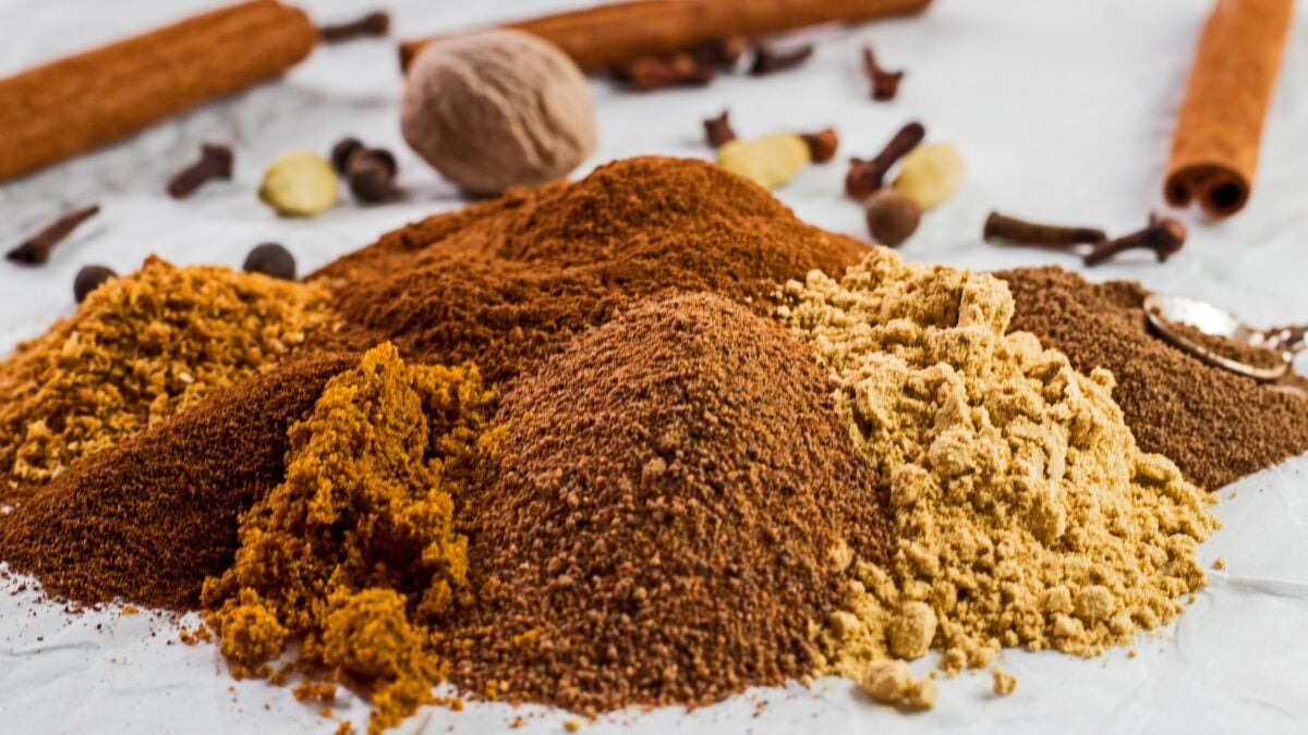 wide image of the ground spices poured onto a white background with whole spices for the pumpkin pie spice in background.