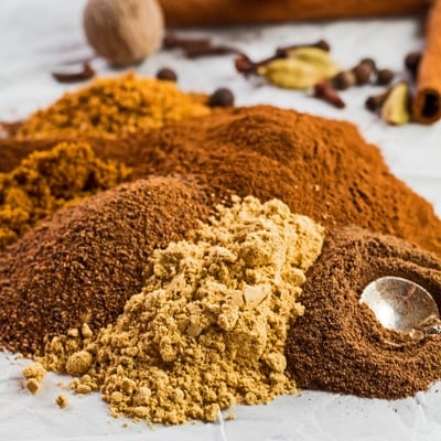 small square image of the ground spices poured onto a white background with whole spices for the pumpkin pie spice in background.