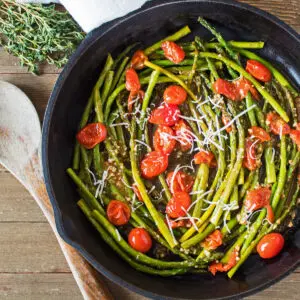 large square image sauteed asparagus and cherry tomatoes in cast iron skillet.