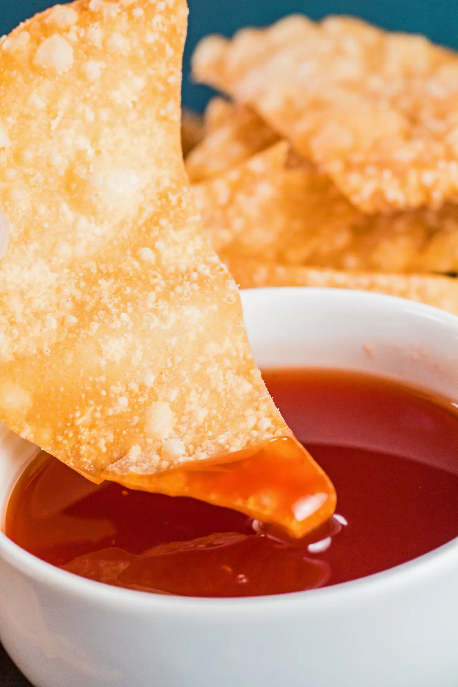 tall closeup of a fried wonton being dipped into the bowl of sweet and sour sauce.
