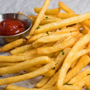 Grande imagem quadrada de batatas fritas congeladas de fritadeira de ar, servidas com ketchup.