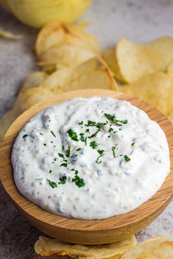 tall image of the french onion dip with chips and onion in background.