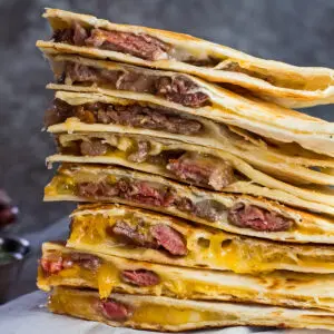 large square image of stacked leftover prime rib quesadillas with condiments in background.