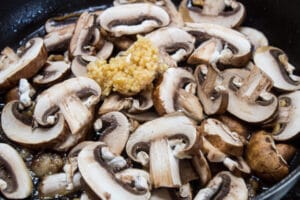 In Scheiben geschnittene Pilze und gehackten Knoblauch in ausgelassenem Fett anbraten.