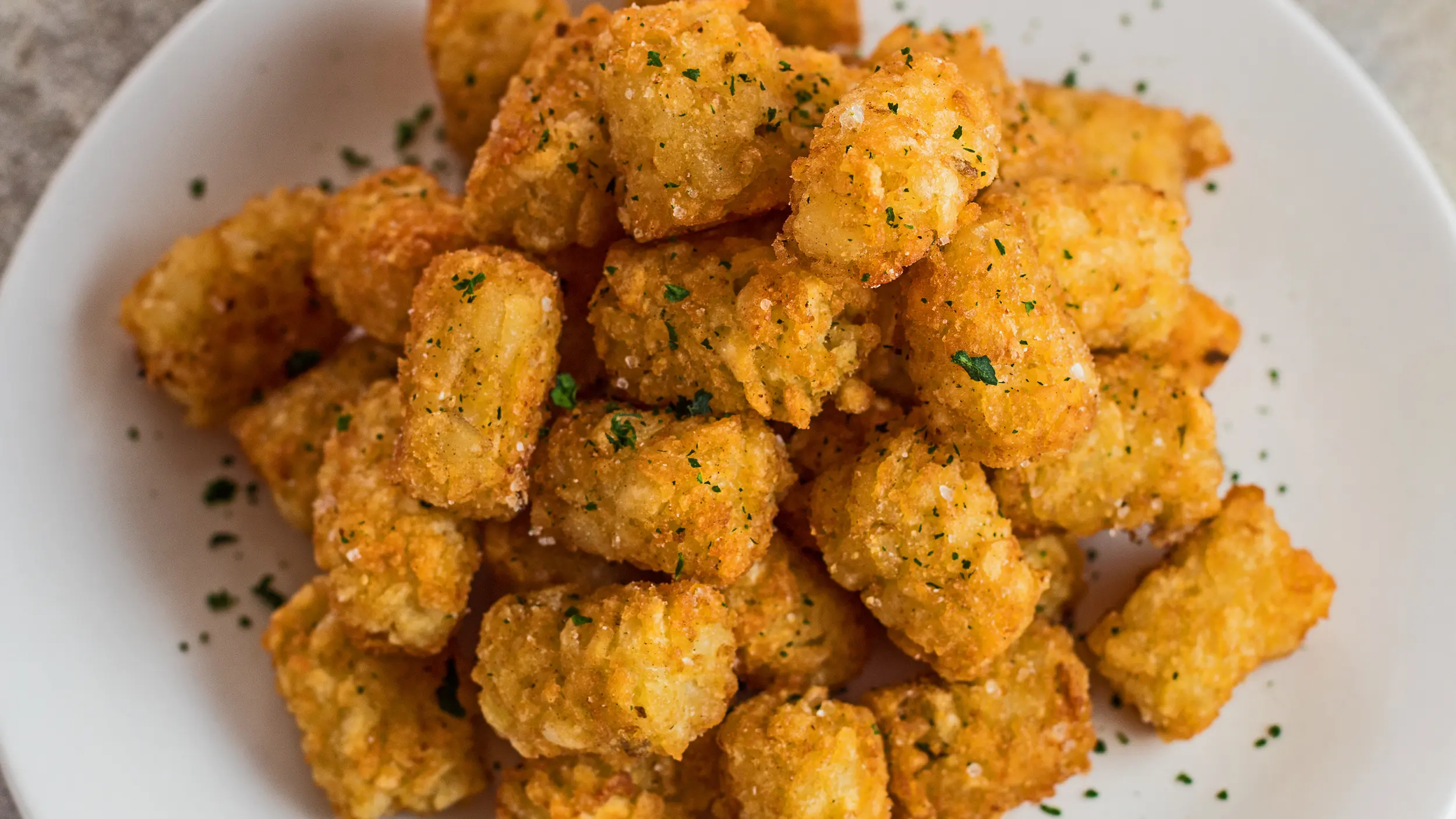 wide angled overhead image of air fryer tater tots on white plate.