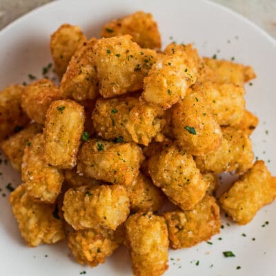 Large square angled overhead image of air fryer tater tots on white plate.