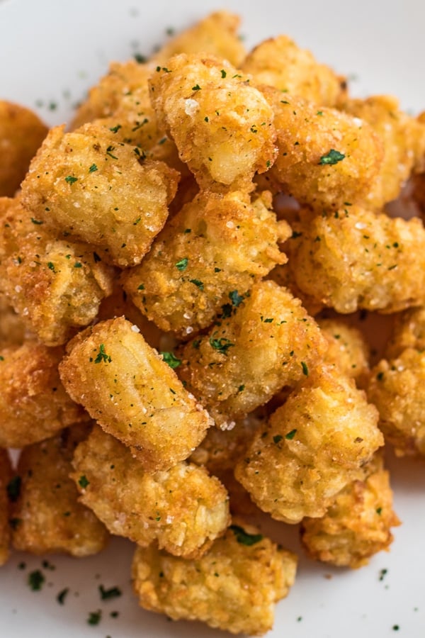 Tall angled overhead image of air fryer tater tots on white plate.