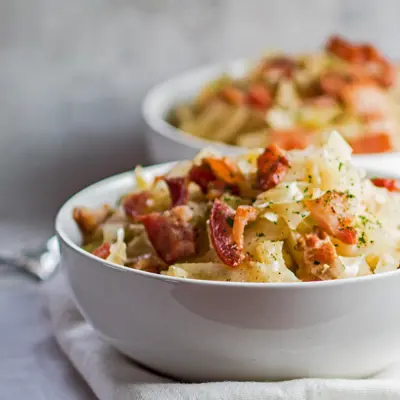 small square sideview of the crockpot cabbage served in a white bowl with extra bacon on top.