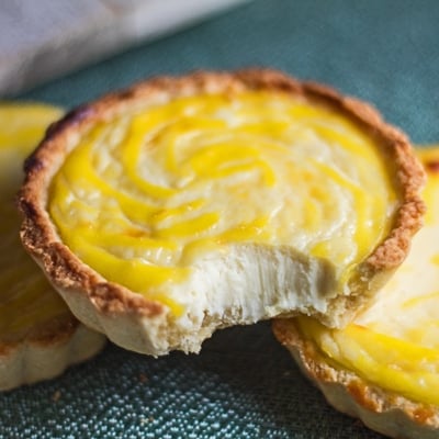 small square closeup image of the hokkaido cheese tarts with a bite showing the creamy texture.