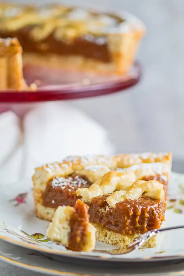 tall closeup image of the pasta frola slice on plate with tart in background.