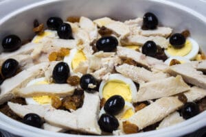 layering the cooked chicken breast meat, raisins, and olives.