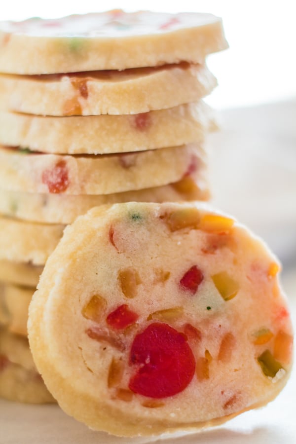 tall closeup image of fruitcake shortbread cookie leaning against stack of cookies in background.