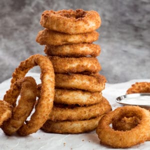 large square image of crispy air fryer frozen onion rings stacked 8 high with dip on the side.