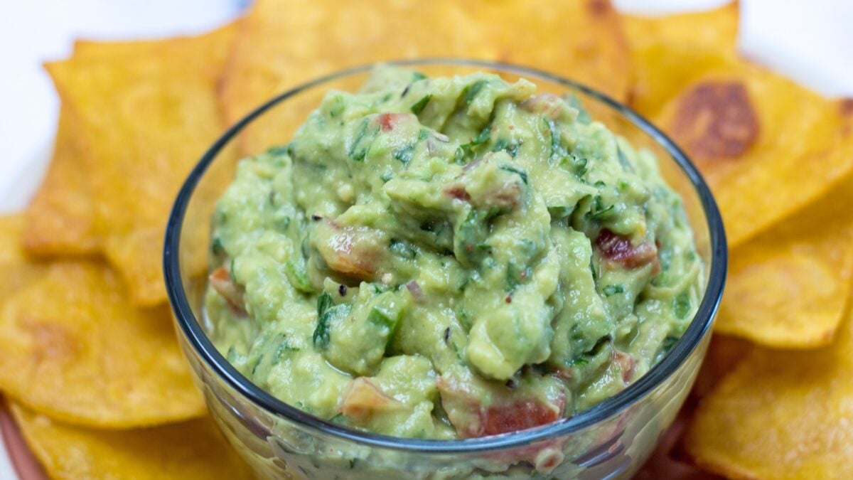 wide image with bowl of guacamole and tortilla chips.