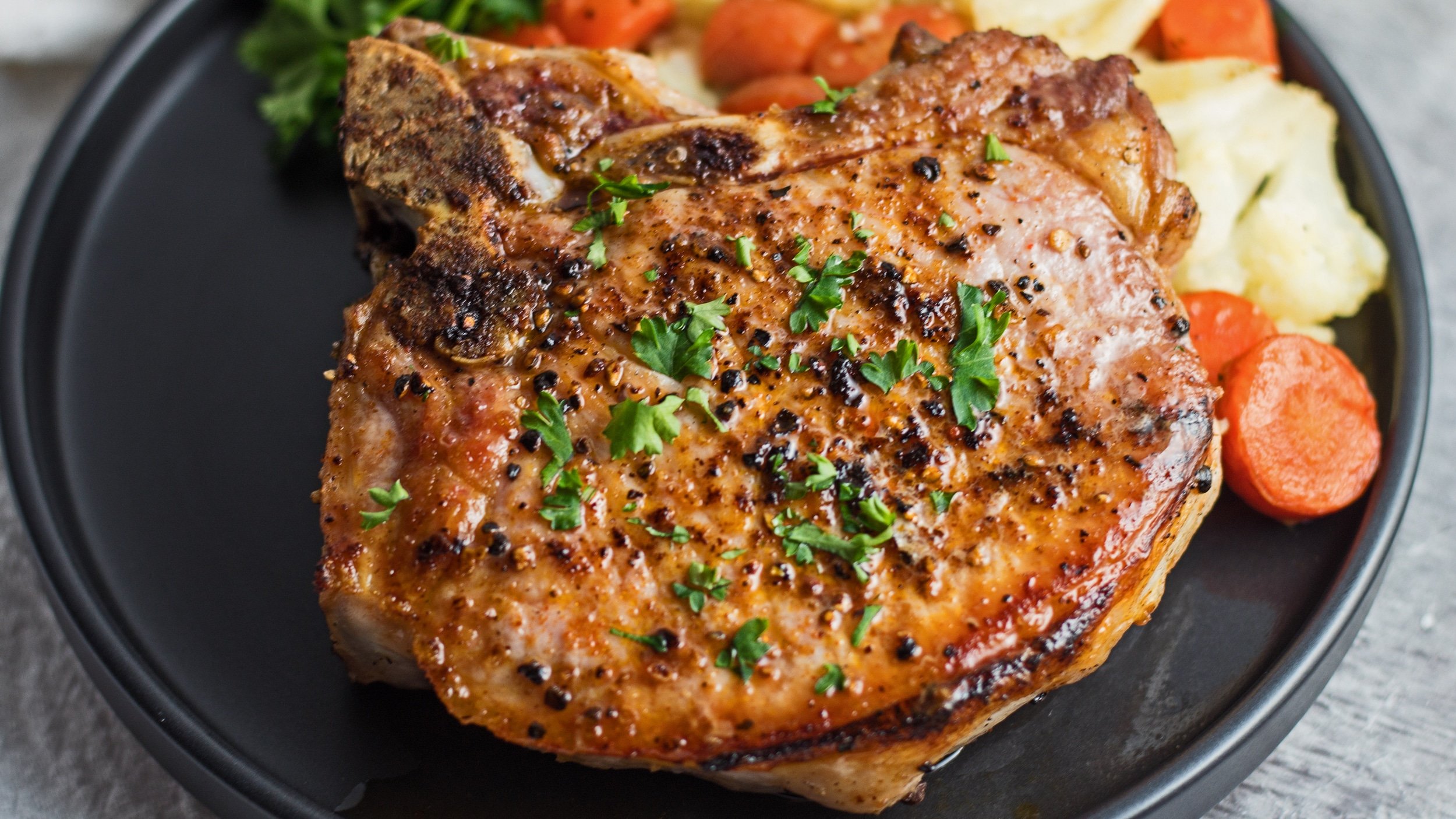 Wide image of cast iron pork chops served with vegetables.