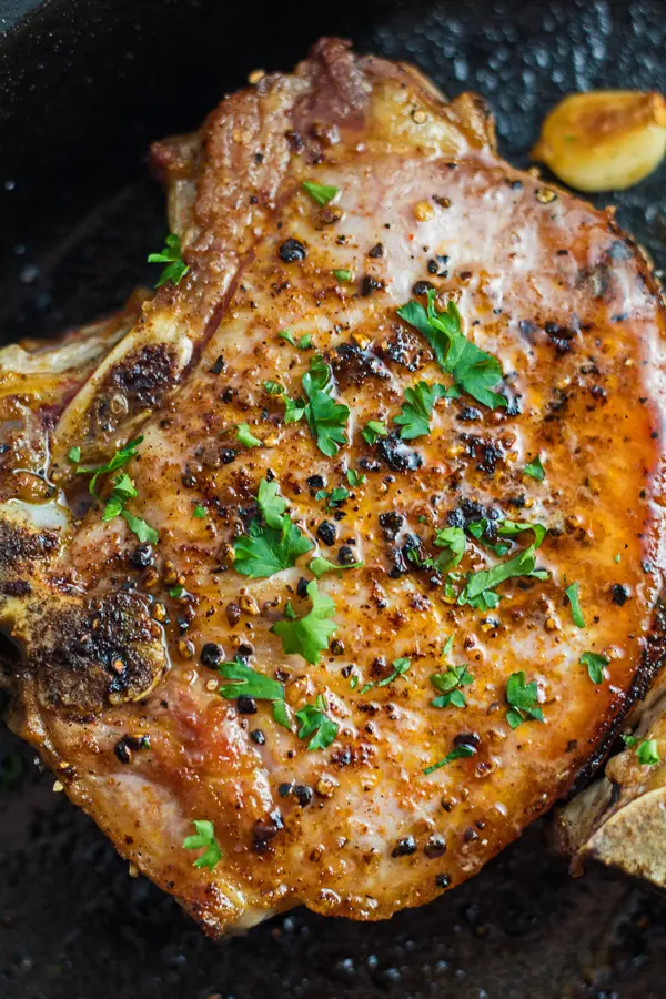 Tall image of the seared cast iron pork chops in the skillet.