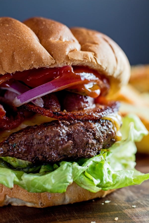 Imagem alta do close up de hambúrguer Wagyu com fatias de batata frita no fundo.